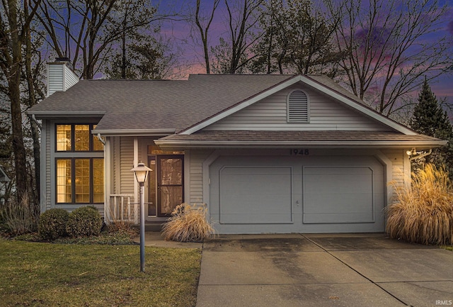 view of front of house featuring a shingled roof, a chimney, concrete driveway, a garage, and a lawn