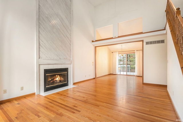 unfurnished living room with visible vents, baseboards, a tiled fireplace, a towering ceiling, and wood finished floors