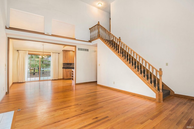 unfurnished living room with visible vents, light wood-style flooring, a high ceiling, an inviting chandelier, and stairs