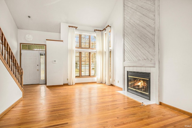 unfurnished living room featuring baseboards, stairway, a tile fireplace, wood finished floors, and high vaulted ceiling