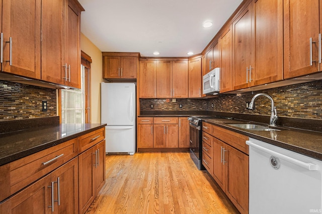 kitchen with light wood finished floors, decorative backsplash, dark stone countertops, white appliances, and a sink