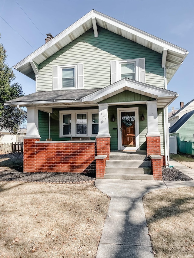 view of front facade featuring brick siding, covered porch, and fence