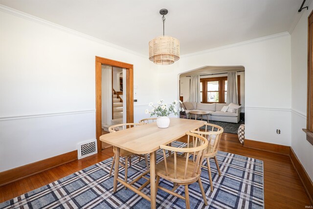 dining room featuring visible vents, baseboards, ornamental molding, wood finished floors, and arched walkways