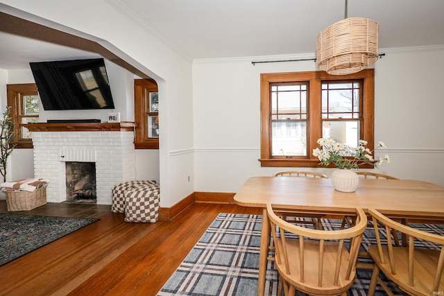 dining area with plenty of natural light, a brick fireplace, wood finished floors, and crown molding