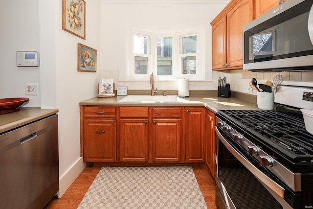 kitchen with light wood-style flooring, a sink, light countertops, appliances with stainless steel finishes, and backsplash