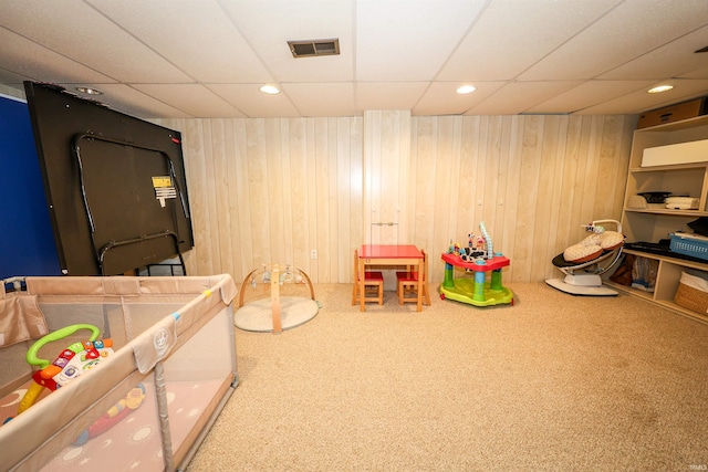 recreation room with visible vents, carpet, wooden walls, and a drop ceiling