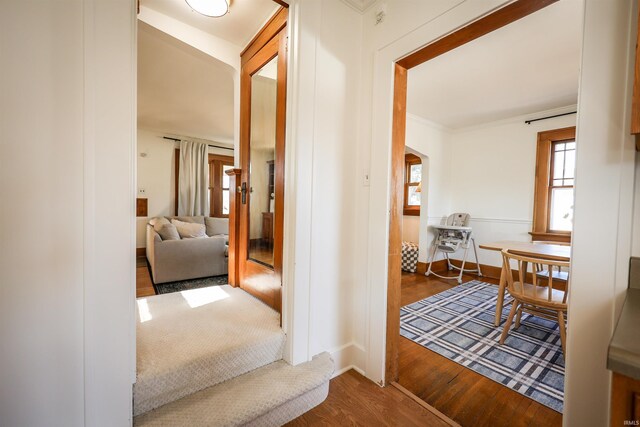 hallway with arched walkways, ornamental molding, and wood finished floors