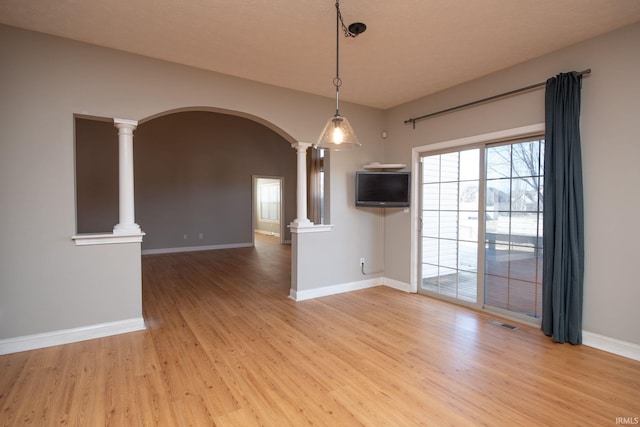 unfurnished room with decorative columns, arched walkways, visible vents, and light wood finished floors