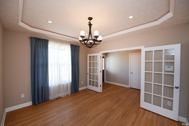 unfurnished room featuring a tray ceiling, baseboards, and light wood-type flooring