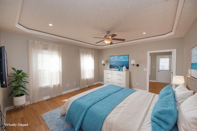 bedroom featuring light wood finished floors, visible vents, a raised ceiling, and baseboards