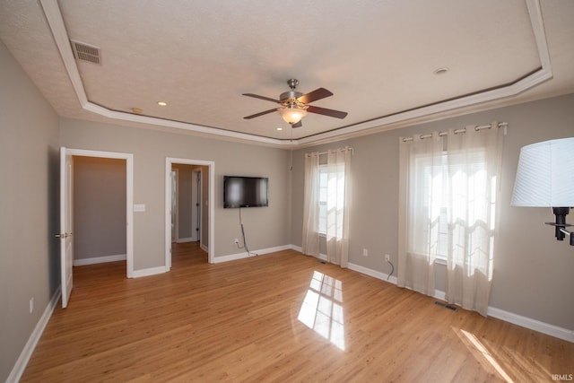 unfurnished bedroom with light wood finished floors, visible vents, a raised ceiling, and baseboards