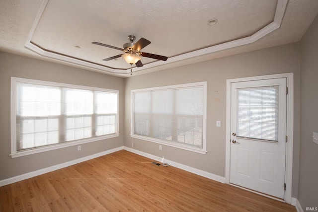 interior space featuring light wood finished floors, a ceiling fan, a raised ceiling, and baseboards