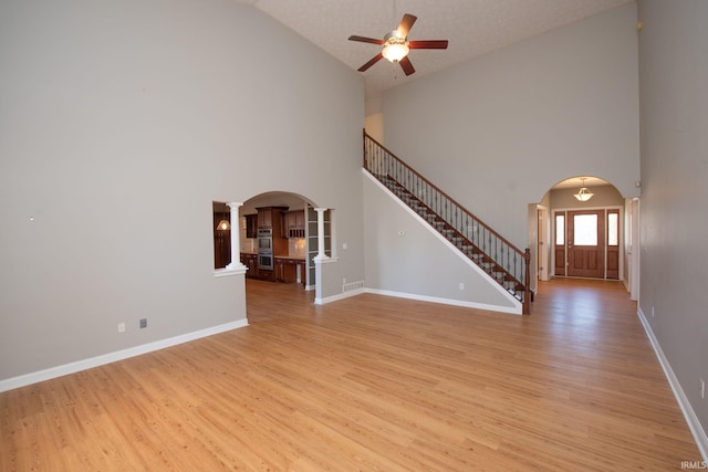 unfurnished living room featuring arched walkways, stairs, and light wood-style floors