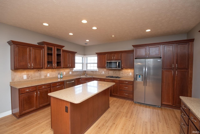 kitchen with a sink, decorative backsplash, appliances with stainless steel finishes, and light wood finished floors