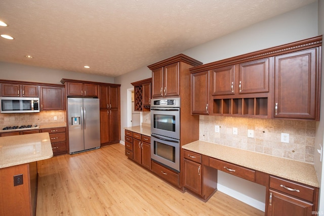 kitchen featuring light wood-type flooring, stainless steel appliances, tasteful backsplash, and built in desk