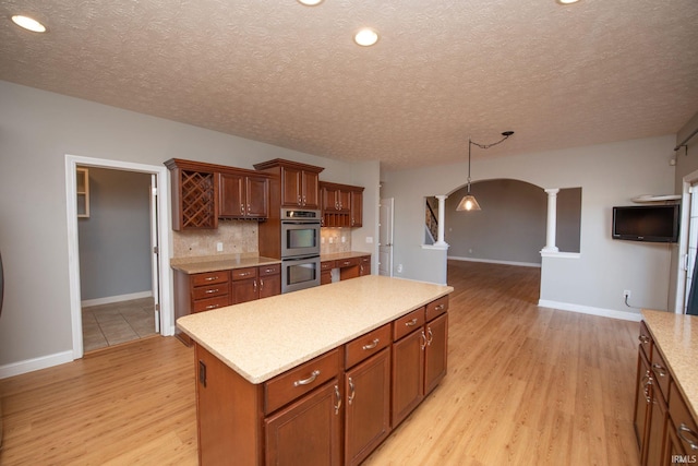 kitchen featuring double oven, arched walkways, ornate columns, and light wood-type flooring