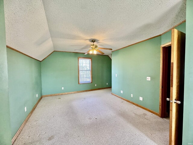 unfurnished room featuring crown molding, baseboards, carpet, vaulted ceiling, and a ceiling fan