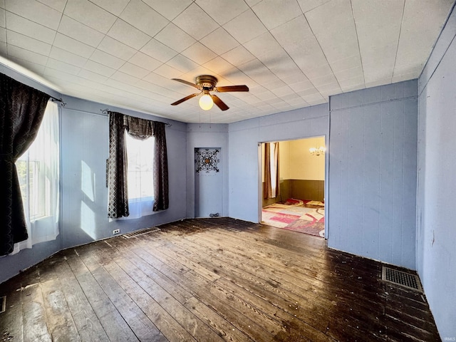 unfurnished room featuring hardwood / wood-style flooring, visible vents, wood walls, and ceiling fan