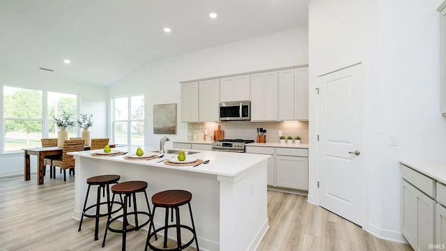 kitchen with a breakfast bar area, light wood finished floors, a kitchen island with sink, stainless steel appliances, and backsplash