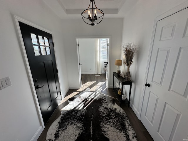 entrance foyer featuring dark wood-type flooring, a notable chandelier, a healthy amount of sunlight, and a raised ceiling