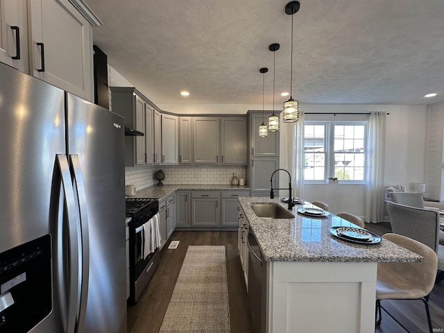 kitchen with backsplash, dark wood-type flooring, light stone countertops, stainless steel appliances, and a sink