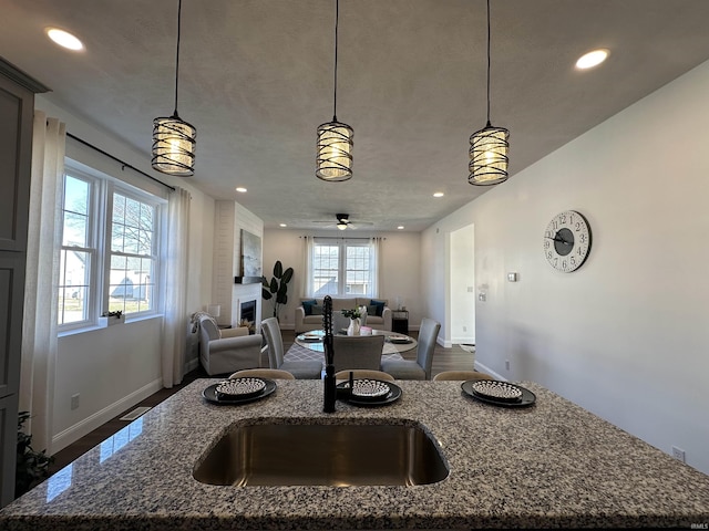 kitchen featuring hanging light fixtures, stone counters, a fireplace, and an island with sink