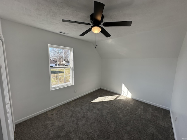 empty room with baseboards, visible vents, vaulted ceiling, a textured ceiling, and dark carpet