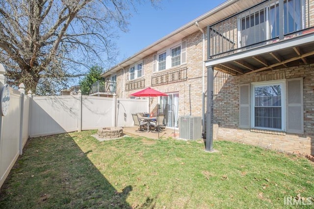 back of property featuring brick siding, a lawn, a fenced backyard, a balcony, and a patio