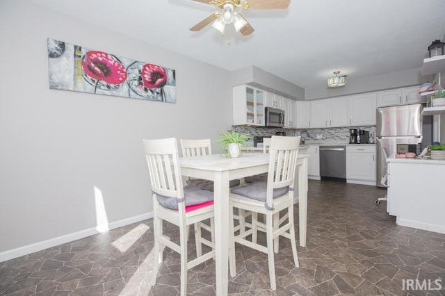 dining area with a ceiling fan, stone finish flooring, and baseboards