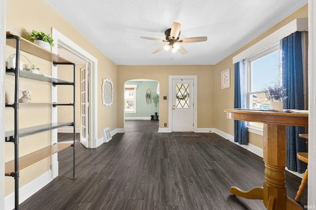 foyer with visible vents, baseboards, dark wood-style floors, arched walkways, and a ceiling fan