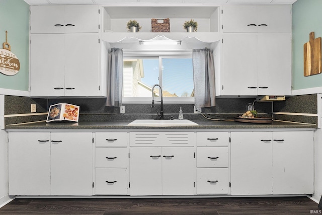 kitchen with dark countertops, white cabinets, and a sink