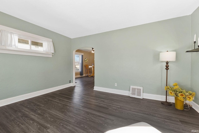 unfurnished room with visible vents, arched walkways, dark wood-style flooring, and baseboards