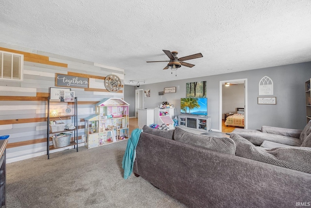 living room with visible vents, a textured ceiling, wood walls, carpet flooring, and ceiling fan