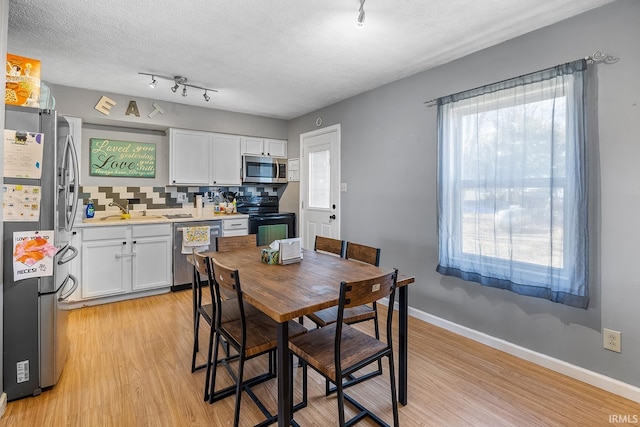 dining room with a wealth of natural light, light wood-type flooring, baseboards, and a textured ceiling