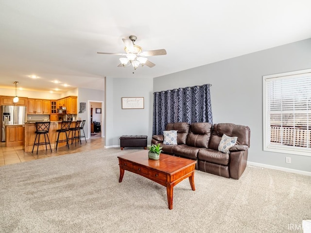 living area with baseboards, light colored carpet, and a ceiling fan