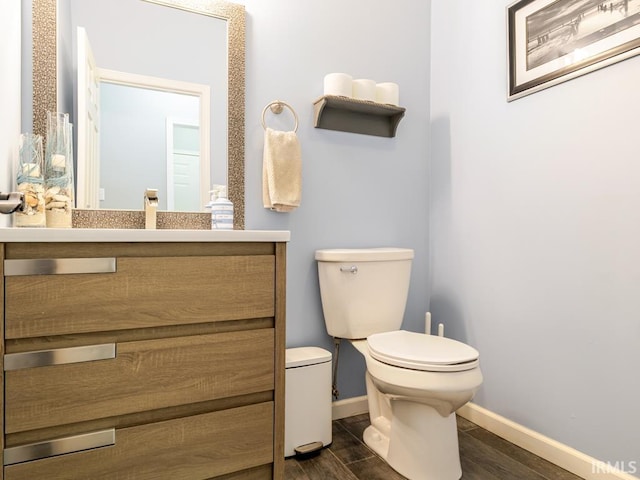 half bathroom with toilet, vanity, baseboards, and wood finished floors