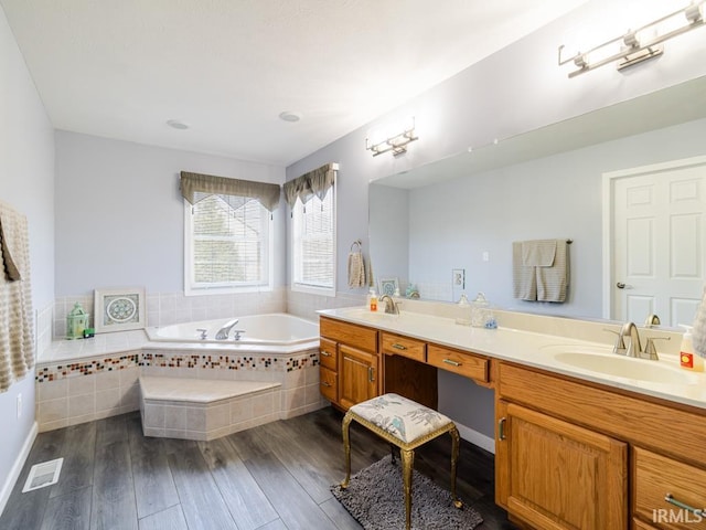 full bath with a sink, a garden tub, wood finished floors, and double vanity