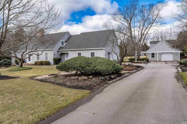 exterior space with a front yard, an outbuilding, roof with shingles, a garage, and aphalt driveway