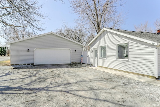 view of property exterior featuring an outbuilding, a detached garage, and roof with shingles