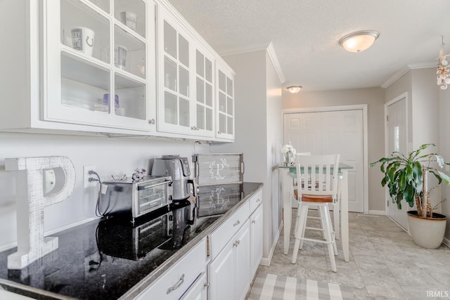 kitchen featuring glass insert cabinets, a textured ceiling, ornamental molding, and white cabinetry