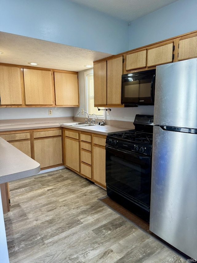 kitchen with black appliances, light wood-style flooring, light brown cabinets, a sink, and light countertops