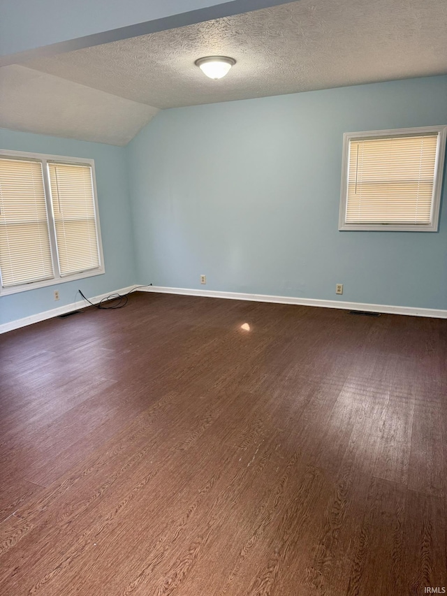 empty room with dark wood finished floors, lofted ceiling, baseboards, and a textured ceiling