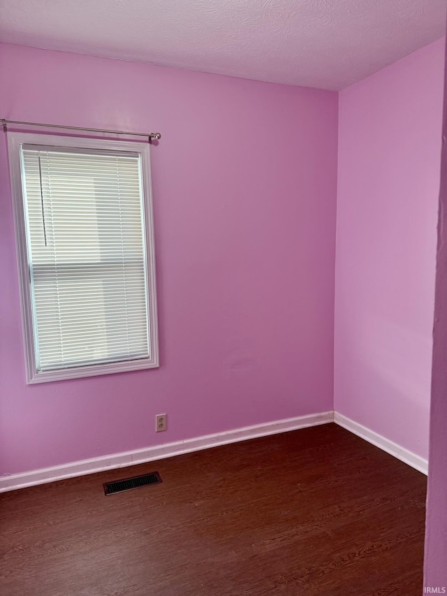 unfurnished room with visible vents, baseboards, dark wood-type flooring, and plenty of natural light