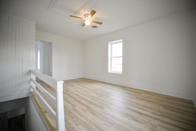 empty room featuring light wood finished floors, visible vents, baseboards, attic access, and a ceiling fan