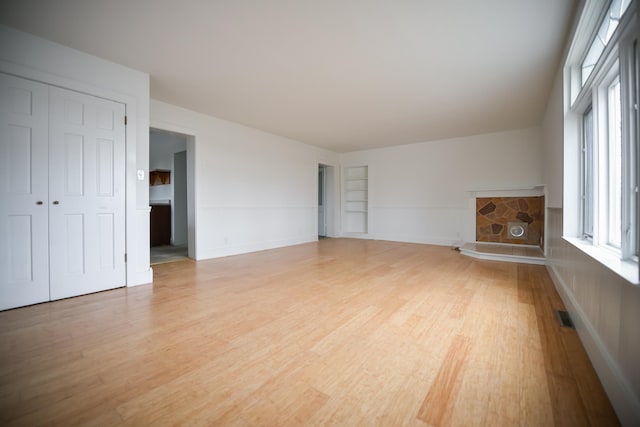 unfurnished living room with a stone fireplace, built in shelves, visible vents, and light wood finished floors