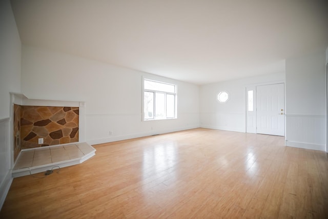 unfurnished living room featuring a wainscoted wall, a fireplace, and light wood-type flooring