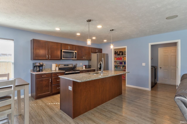 kitchen with light wood-style flooring, an island with sink, a sink, appliances with stainless steel finishes, and a textured ceiling