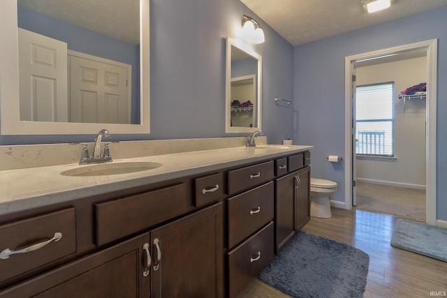 full bathroom featuring double vanity, wood finished floors, toilet, and a sink