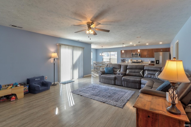 living area with visible vents, baseboards, ceiling fan, wood finished floors, and a textured ceiling