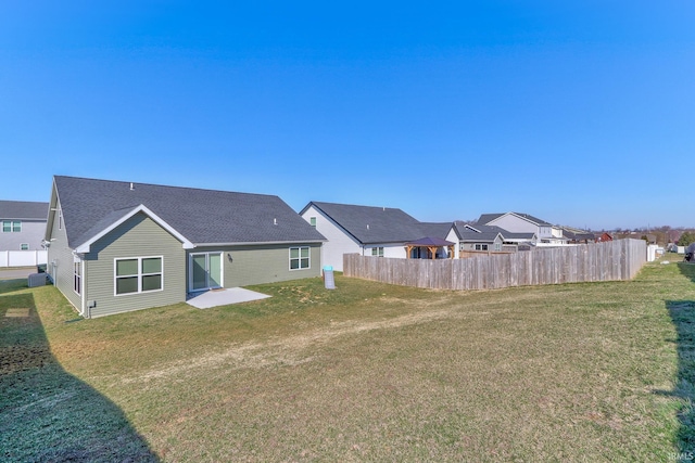 rear view of property with a shingled roof, a yard, and fence